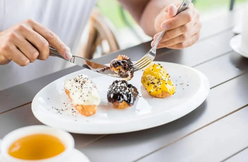 Person enjoying assorted gourmet eclairs on a white plate, depicting food indulgences.